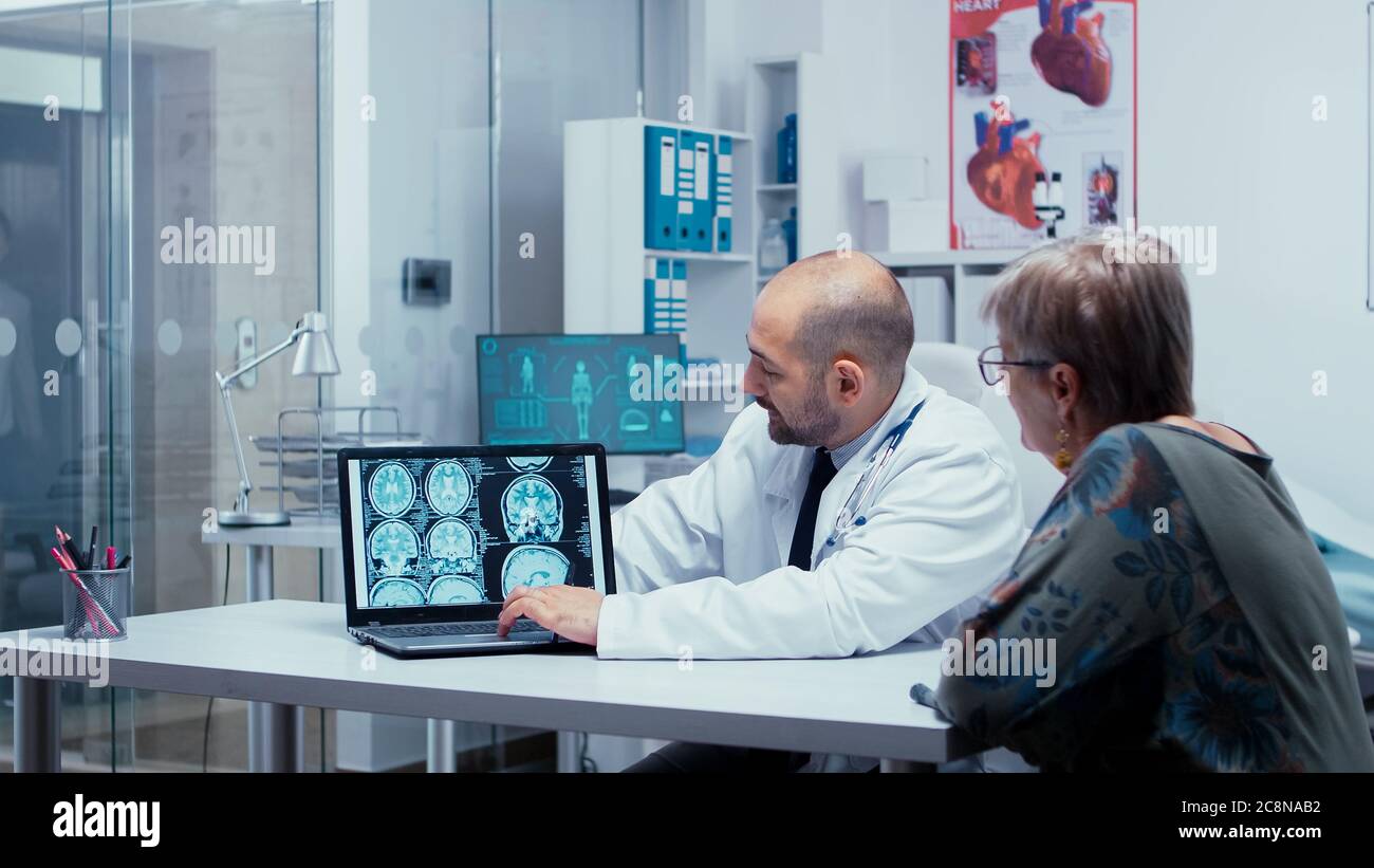 Nell'ufficio dei medici parlare di scansioni cerebrali, TC, RM e scansione  radiologica sullo schermo del computer portatile per pazienti anziani. La  diagnosi cerebrale, la TC, la RM o i raggi X di