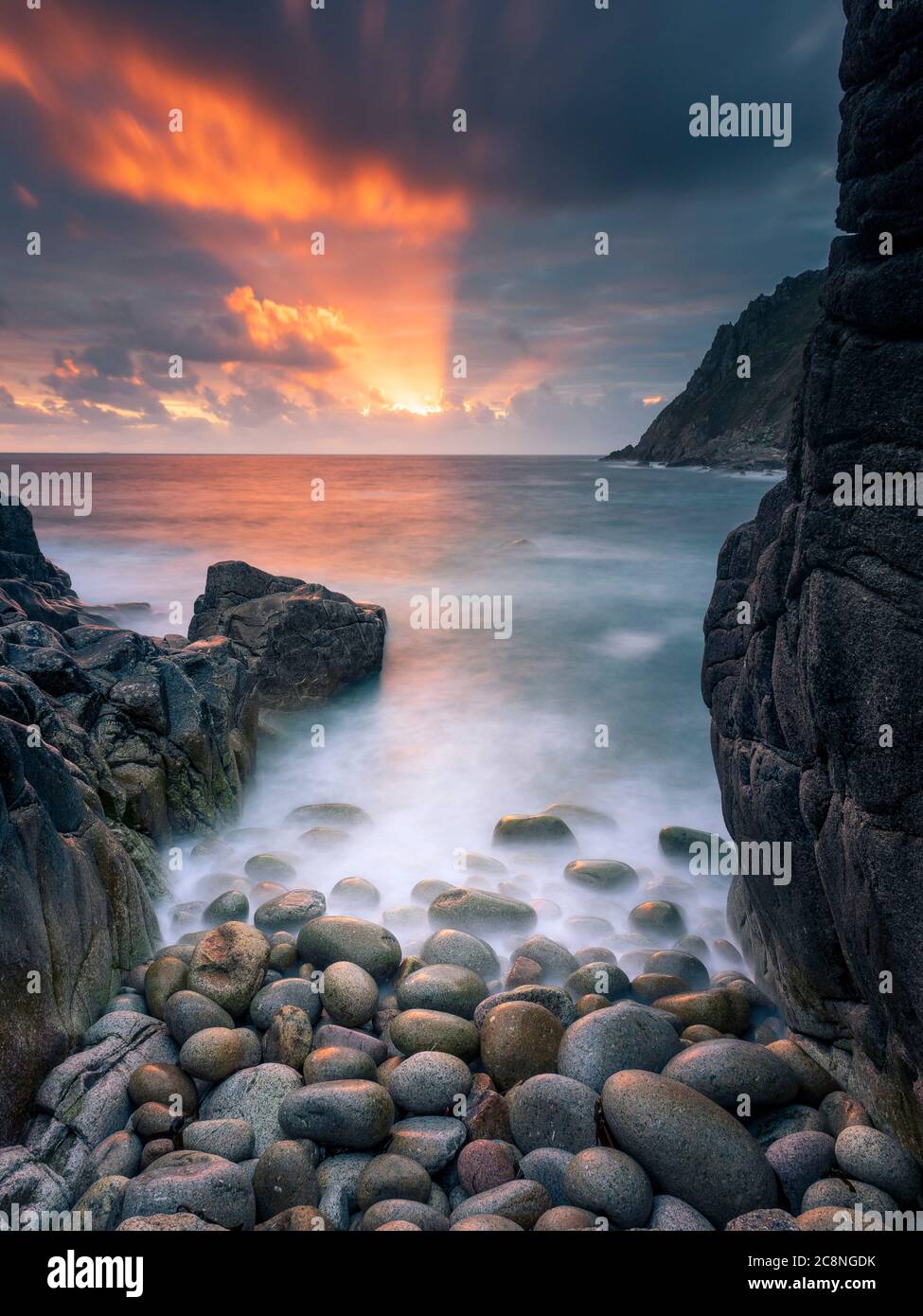 Raggi di sole che illuminano le nuvole in una baia nascosta vicino a Porth Nanven al tramonto. Foto Stock