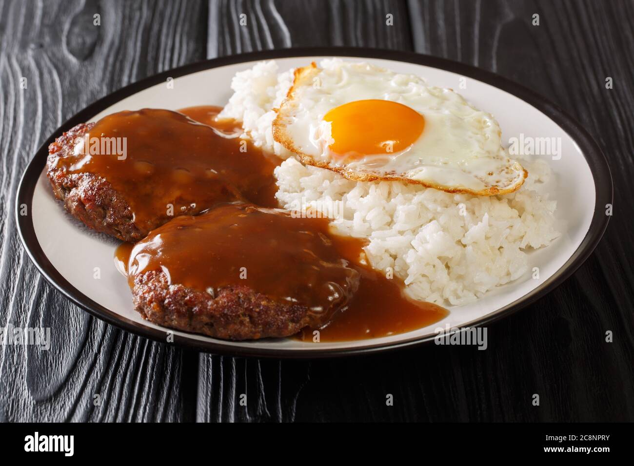 Il Loco moco è una cucina hawaiana preparata con riso bianco con un polpettine di hamburger, uovo con il lato soleggiato in alto e sugo di carne marrone da vicino su un piatto sul tavolo. Foto Stock