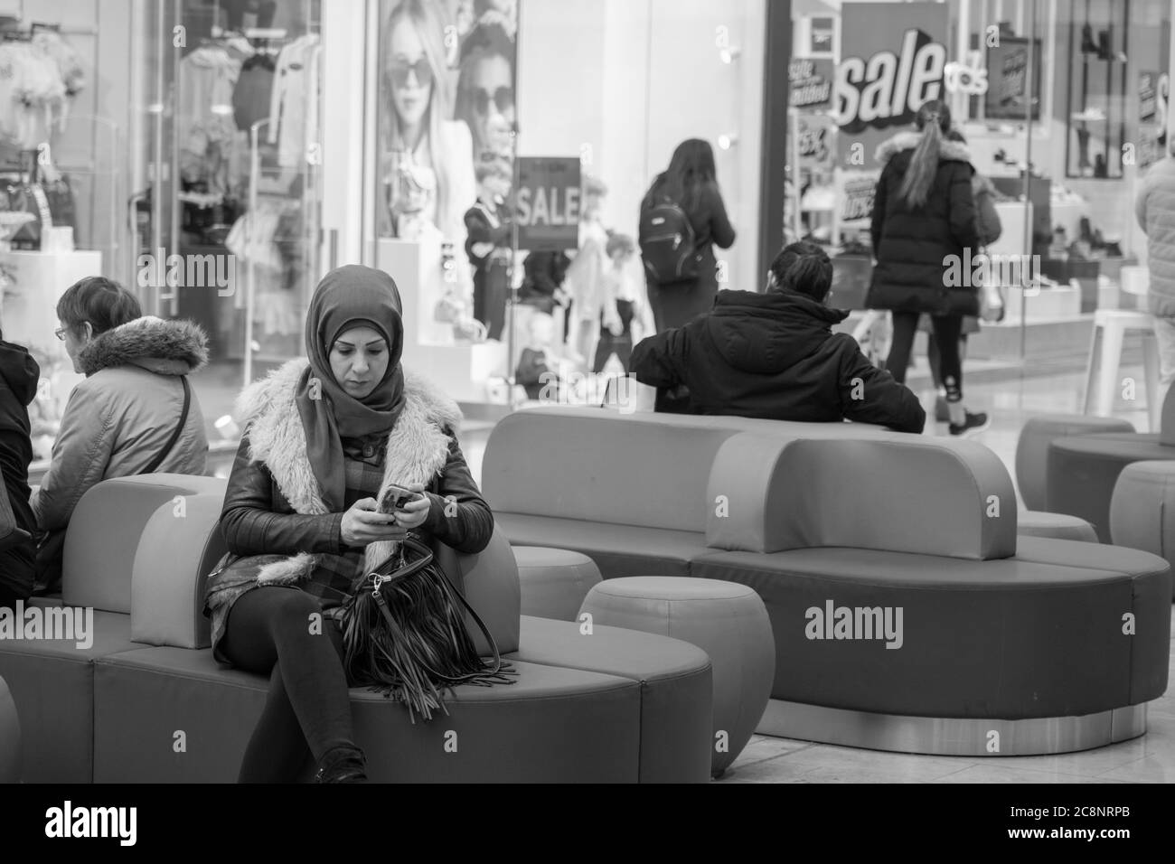 Donna musulmana seduta in un sedile con una sciarpa testando sul suo cellulare, Bradford, West Yorkshire, Inghilterra, Regno Unito. Foto Stock