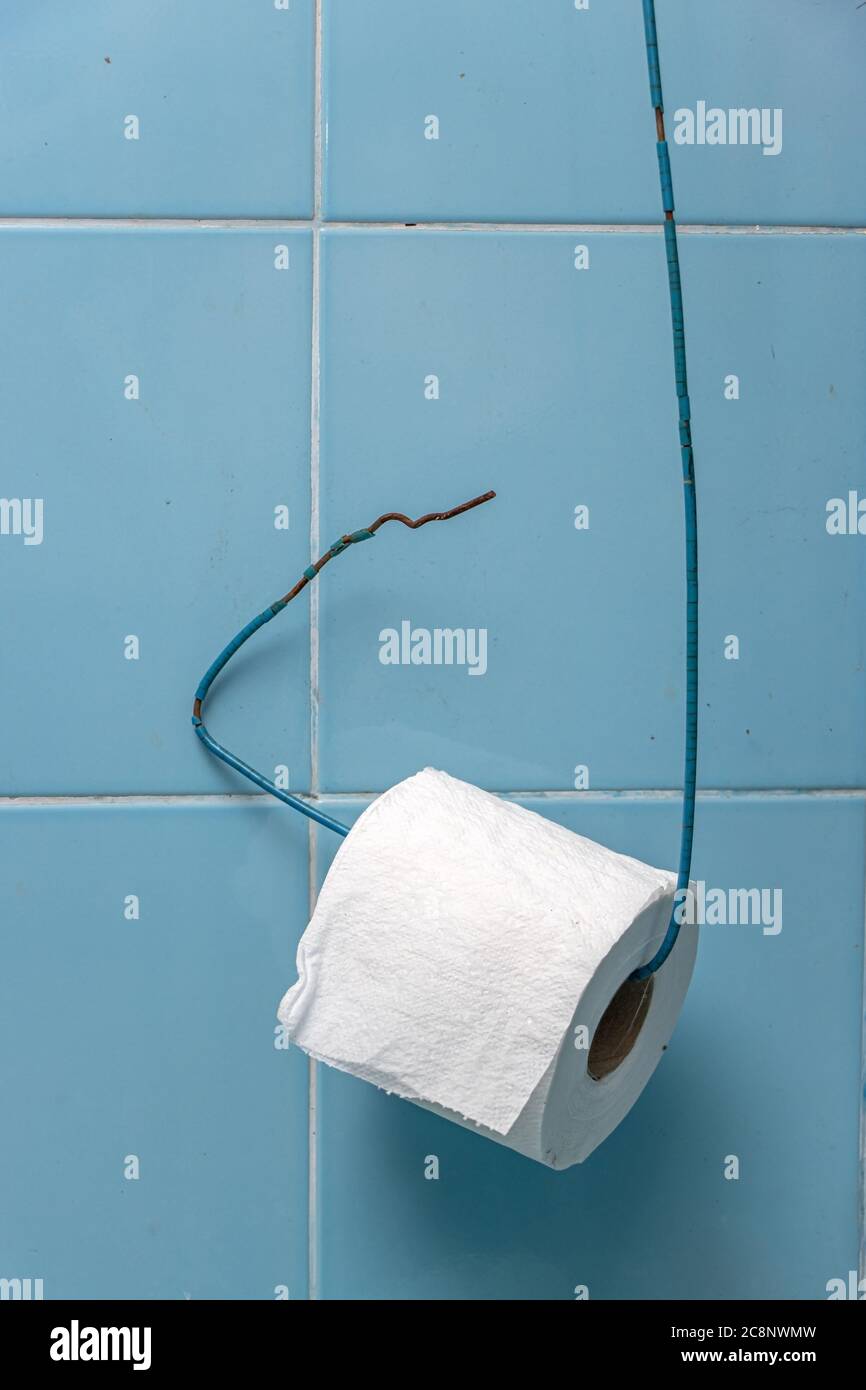 Un rotolo di carta igienica è appeso su un filo di una parete di piastrelle blu. Semplice porta carta igienica in bagno. Foto Stock