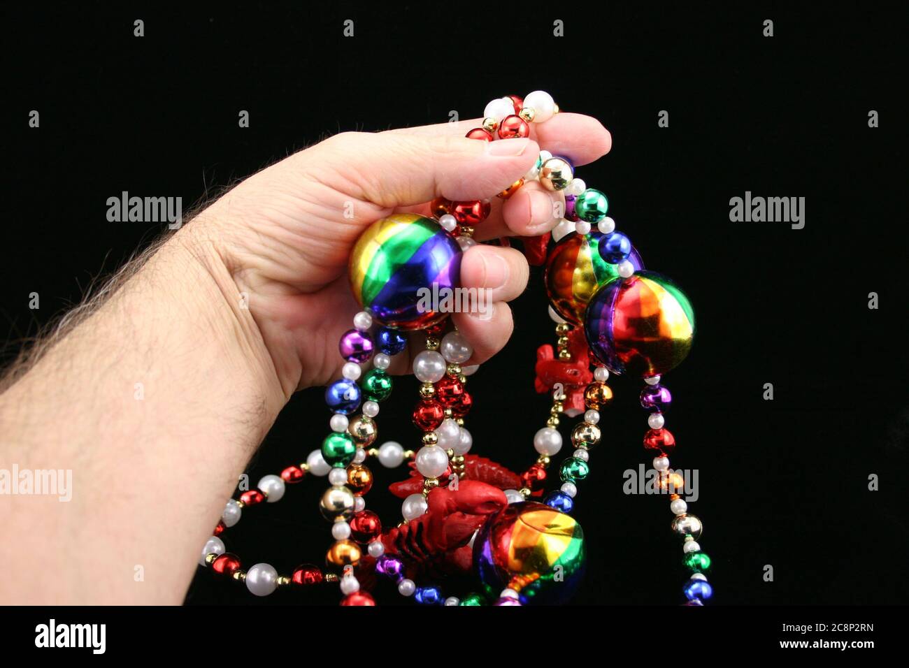 Mano della donna che tiene le perle di Mardi Gras su uno sfondo nero. Foto Stock