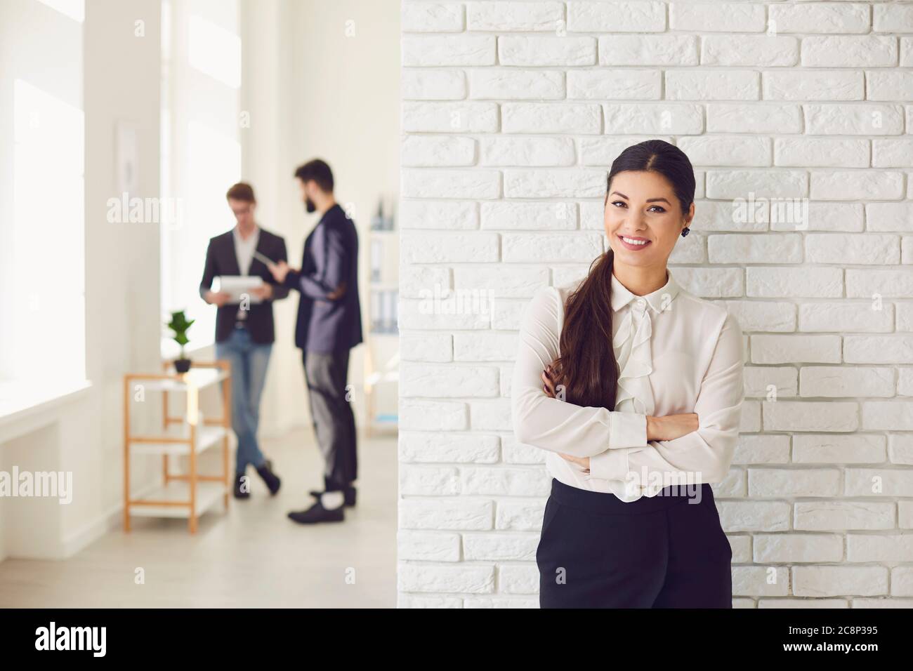 Donna d'affari latina ispanica sorridente mentre si trova in un ufficio bianco contro un muro bianco. Foto Stock