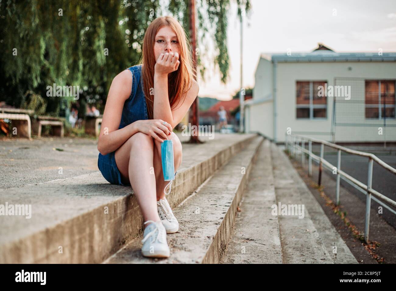 Ragazza teen carina che tiene una maschera nelle sue mani, che guarda infastidita. Protezione da coronavirus Foto Stock