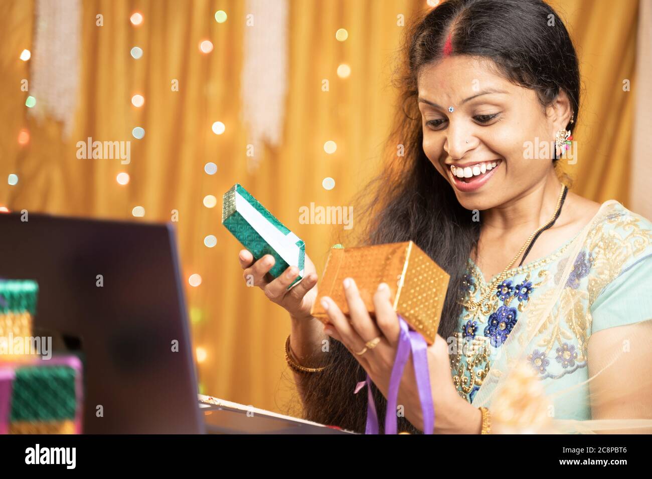 Happy Excited Donna apertura dono davanti al portatile durante la videochiamata o chat alla cerimonia del festival Raksha Bandhan - concetto di relazioni a distanza Foto Stock