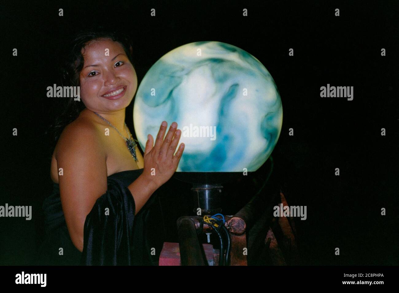 giovane donna indonesiana appoggiata su un globo illuminato durante una serata fuori a seminyak bali indonesia 2002 Foto Stock