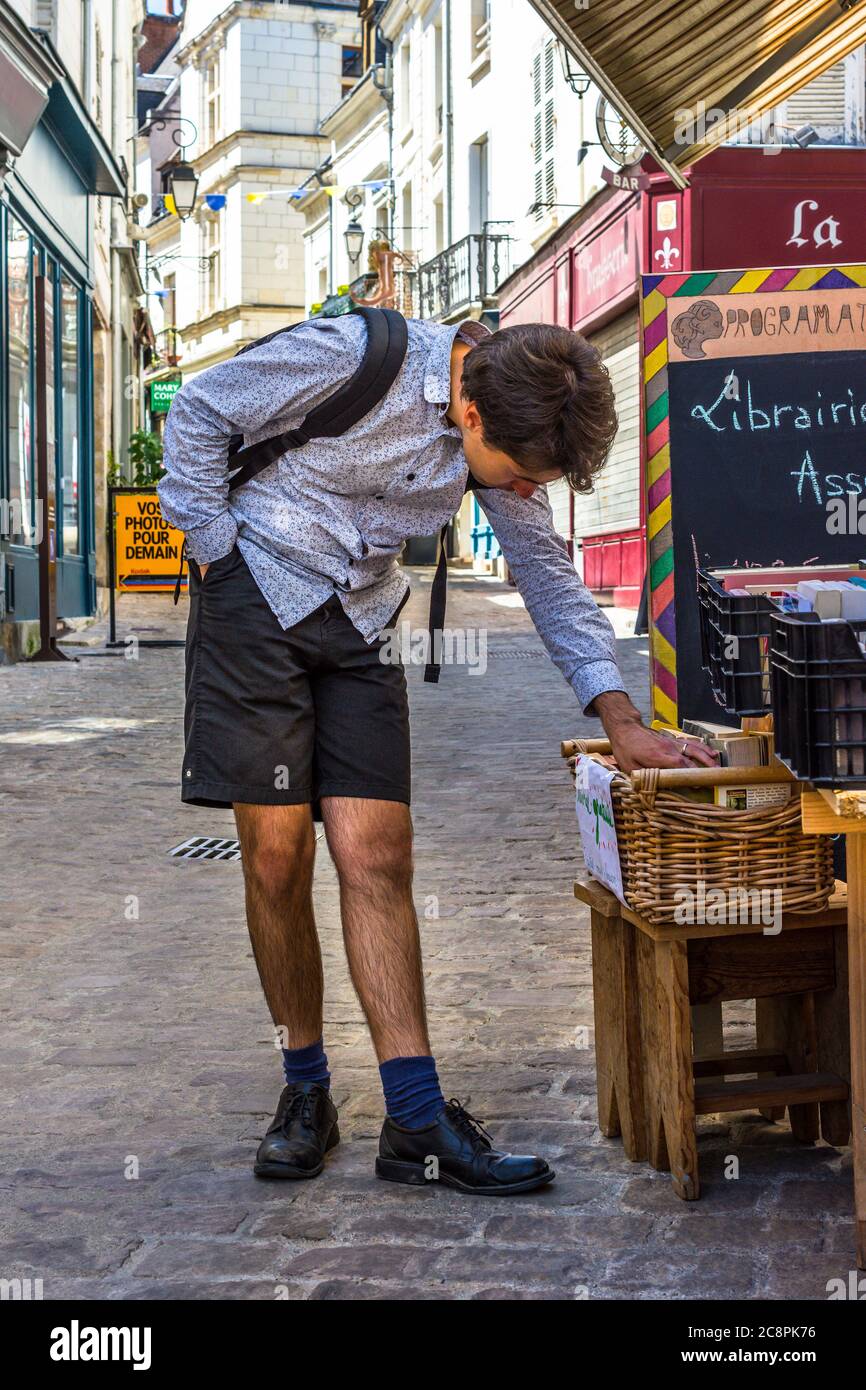 Giovane uomo che naviga libri di seconda mano fuori libreria su strada stretta della città, Loches, Indre-et-Loire, Francia. Foto Stock