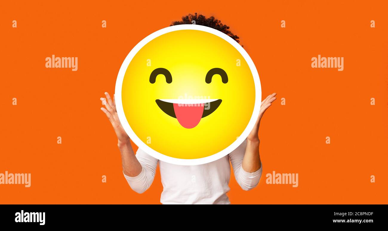 Uomo nero bushy che tiene felice emoji cheeky emoticon davanti alla testa Foto Stock