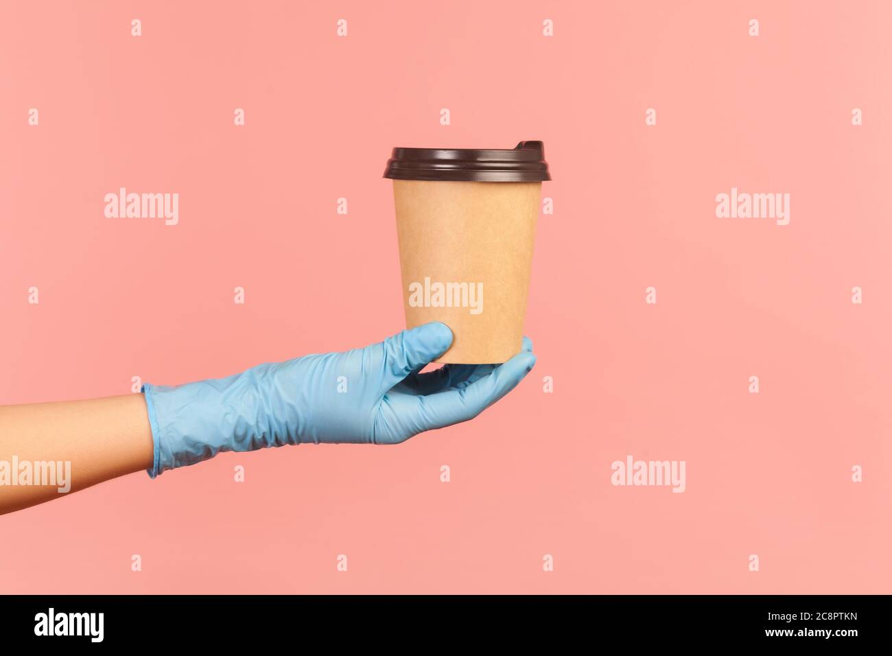 Profilo Vista laterale primo piano della mano umana in guanti chirurgici blu che tengono in mano e mostrano una tazza di tazza da takeaway calda. Interno, studio shot, isolat Foto Stock