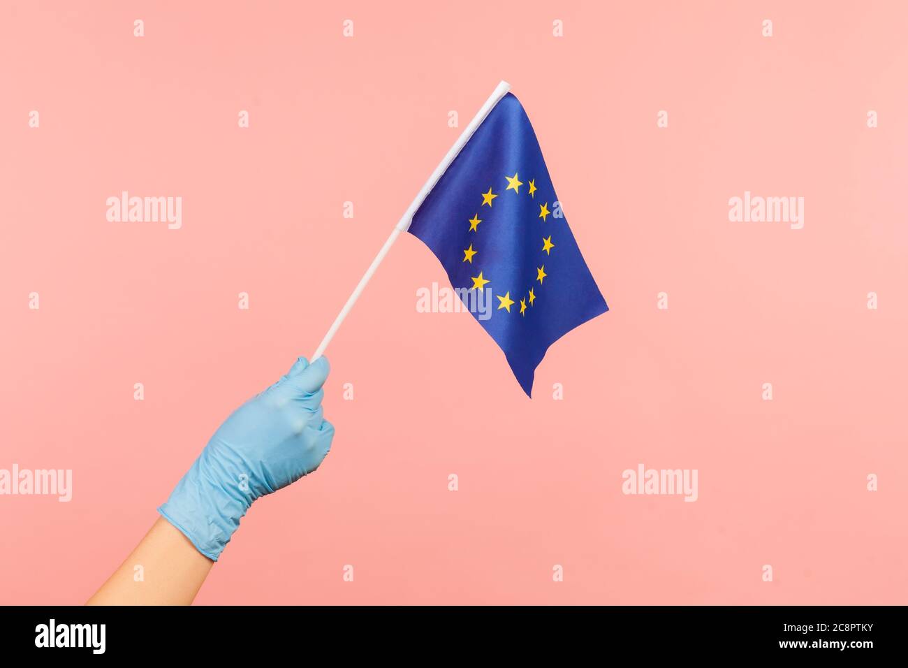 Profilo Vista laterale primo piano della mano umana in guanti chirurgici blu con bandiera di Unione Eroupea. Interno, studio shot, isolato su sfondo rosa. Foto Stock
