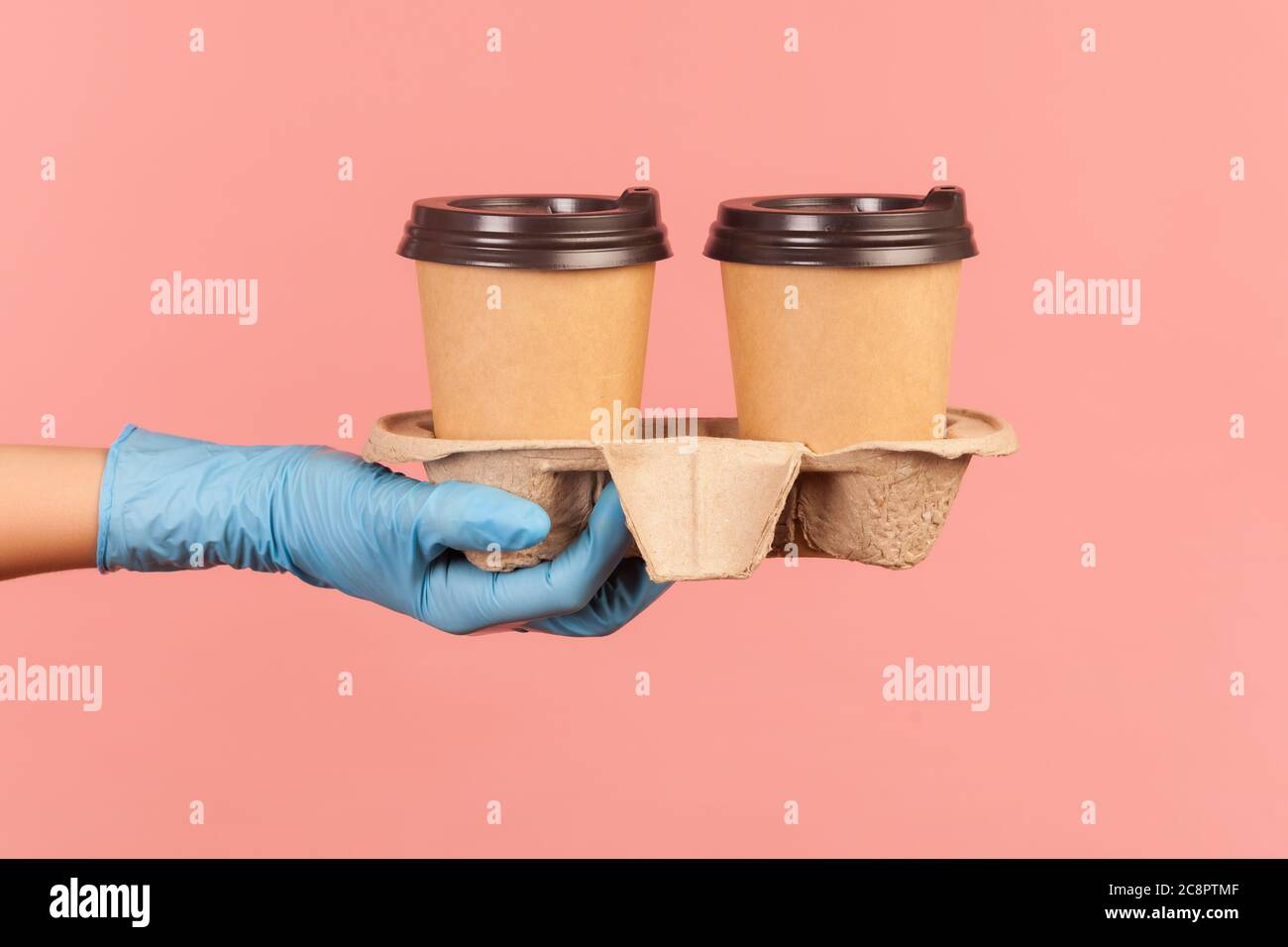 Profilo Vista laterale primo piano della mano umana in guanti chirurgici blu che tengono e mostrano tazze di tazza calda da asporto in mano. Interno, studio shot, isola Foto Stock