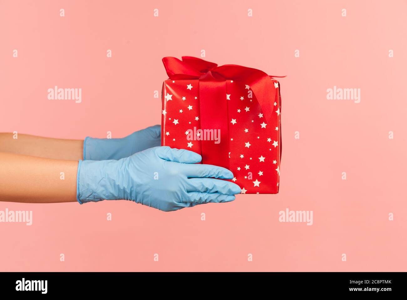 Profilo Vista laterale primo piano della mano umana in guanti chirurgici blu con confezione regalo rossa. Concetto di condivisione, donazione o consegna. Interno, studio shot, isolamento Foto Stock