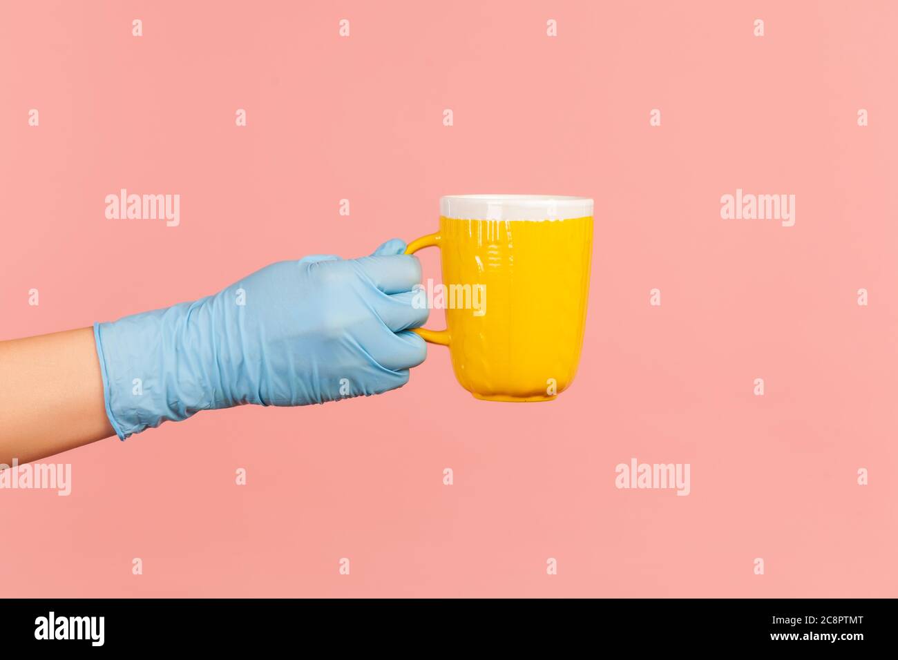 Profilo Vista laterale primo piano della mano umana in guanti chirurgici blu che tengono in mano una tazza gialla di bevanda calda. Interno, studio shot, isolato Foto Stock