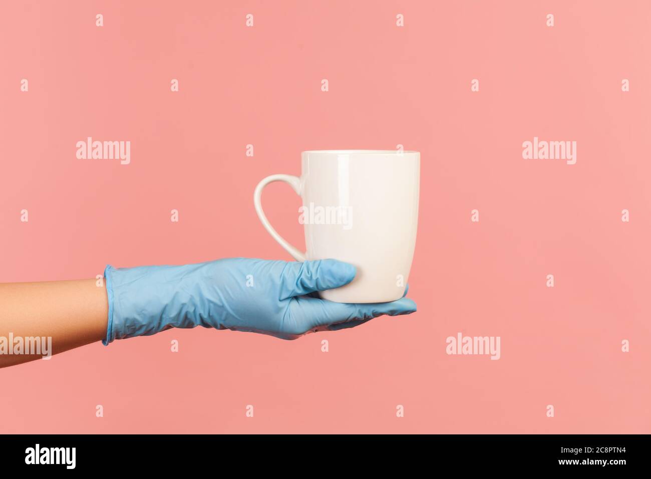 Profilo Vista laterale primo piano della mano umana in guanti chirurgici blu che tengono in mano una tazza bianca di bevanda calda. Interno, studio shot, isolato su p. Foto Stock