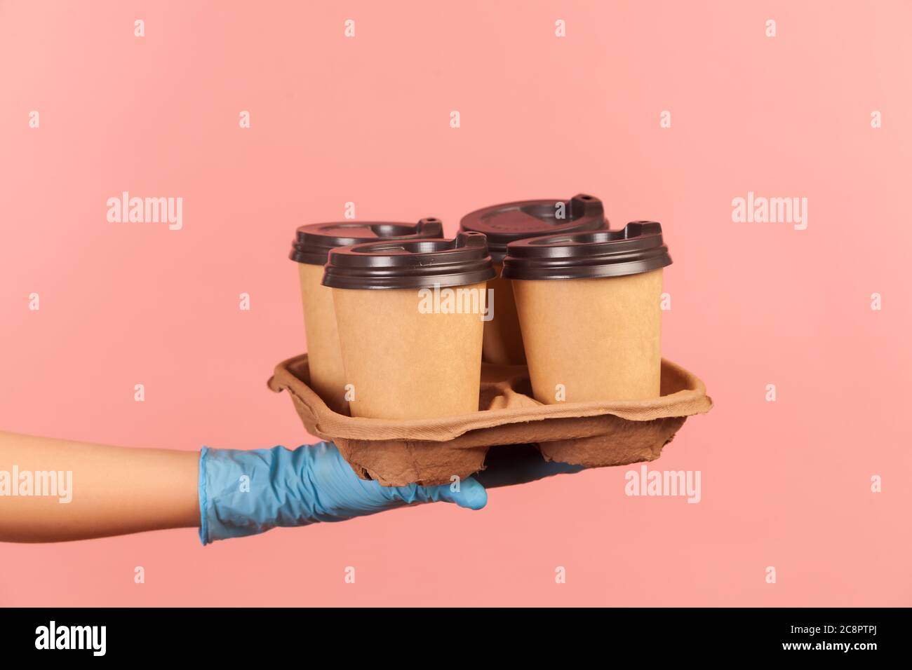 Profilo Vista laterale primo piano della mano umana in guanti chirurgici blu che tengono e mostrano tazze di tazza calda da asporto in mano. Interno, studio shot, isola Foto Stock