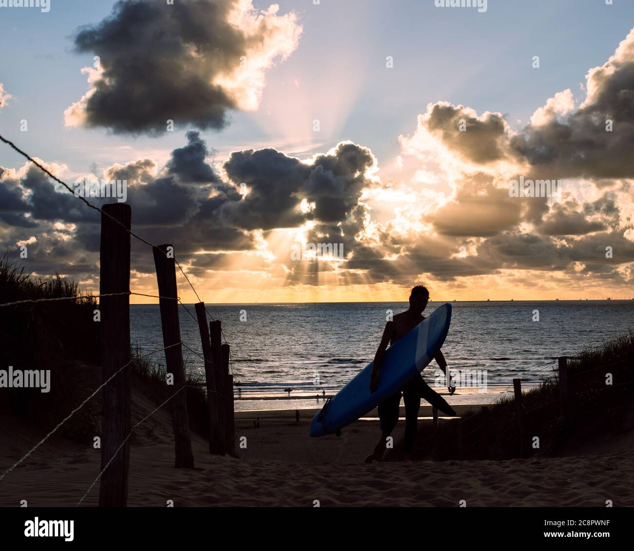 Surfista che cammina con la sua tavola in salita durante il tramonto Foto Stock