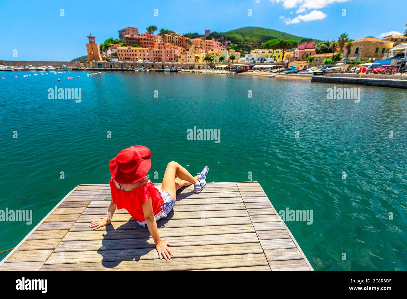 Donna caucasica che riposa e prende il sole sul molo nel porto di Rio Marina dell'isola d'Elba in costume rosso. Ragazza turistica lifestyle in viaggio di vacanza in Italia Foto Stock