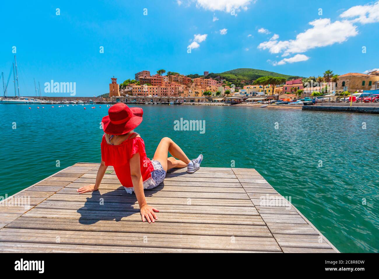 Donna turistica che prende il sole sul molo nel porto di Rio Marina dell'isola d'Elba in costume rosso. Ragazza turistica lifestyle in viaggio di vacanza in Italia, Europa. Rio Foto Stock