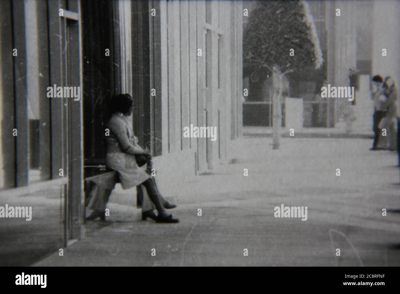 Fine anni '70 vintage nero e bianco stile di vita fotografia di una donna che riposa su una panchina sul marciapiede. Foto Stock