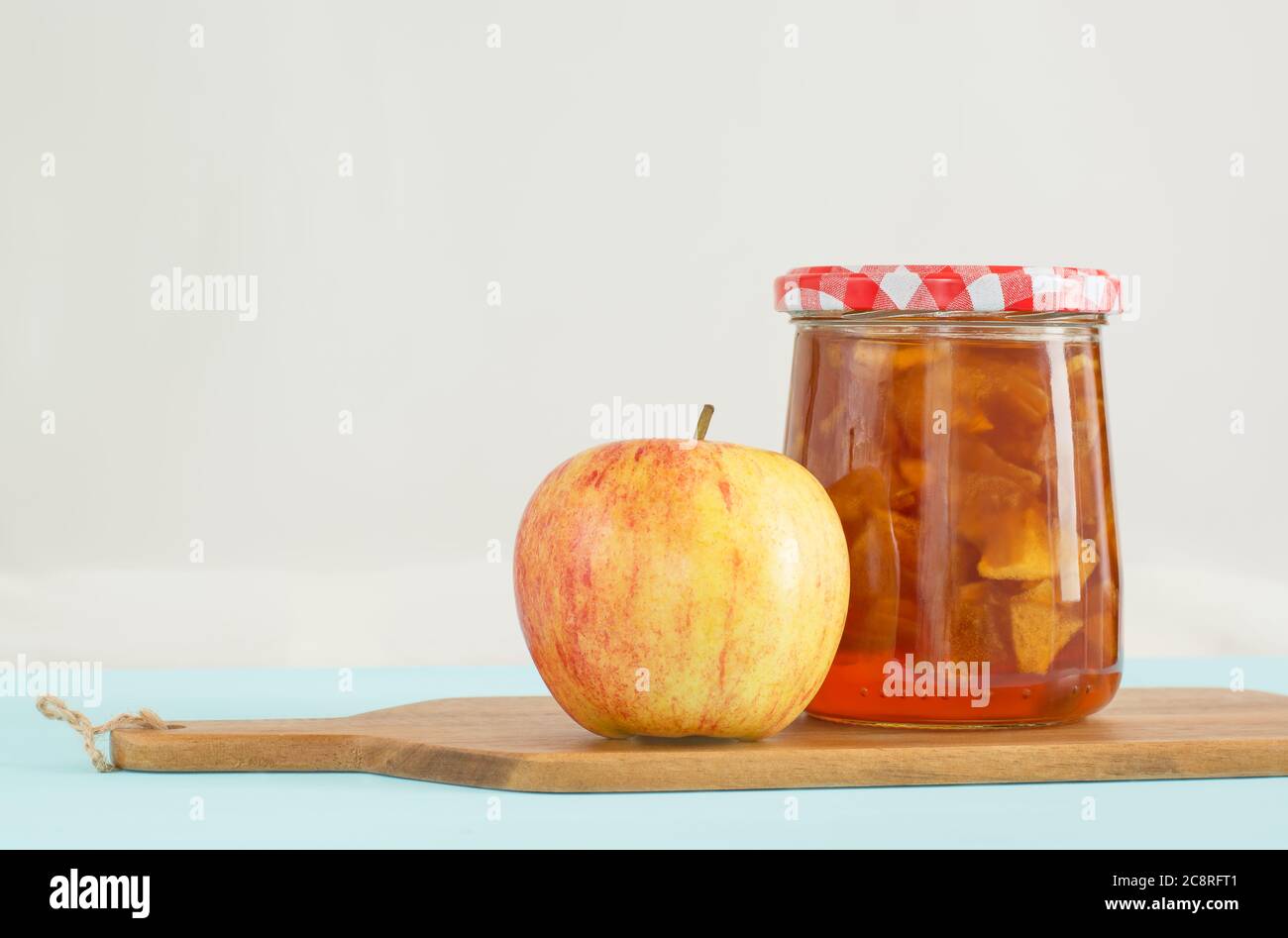 Vasetto di vetro di marmellata di mele fatta in casa con coperchio a scacchi e mela sul tavolo da cucina Foto Stock