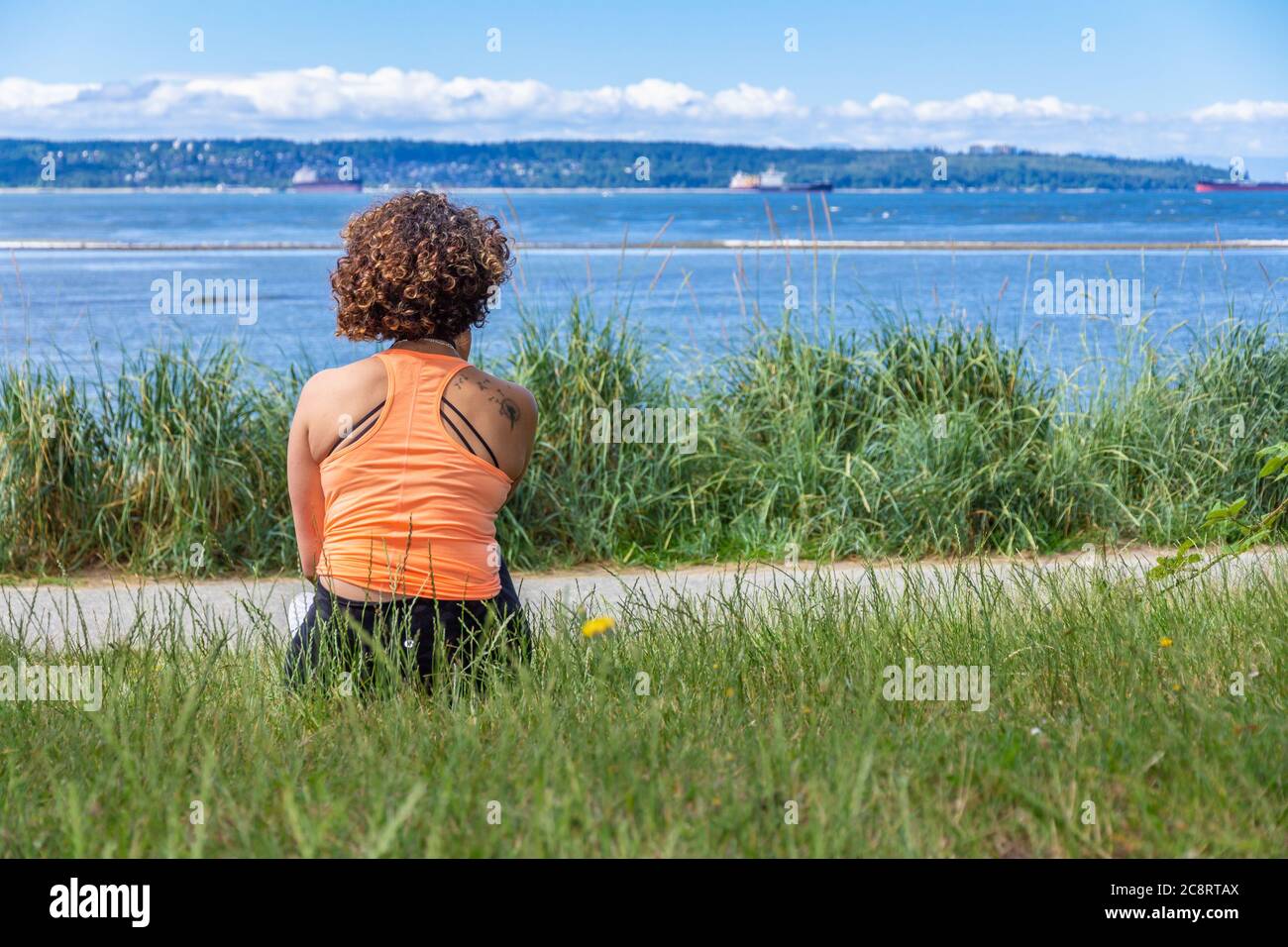 Vista posteriore di una giovane donna con la parte superiore arancione dell'halter che guarda all'oceano Foto Stock