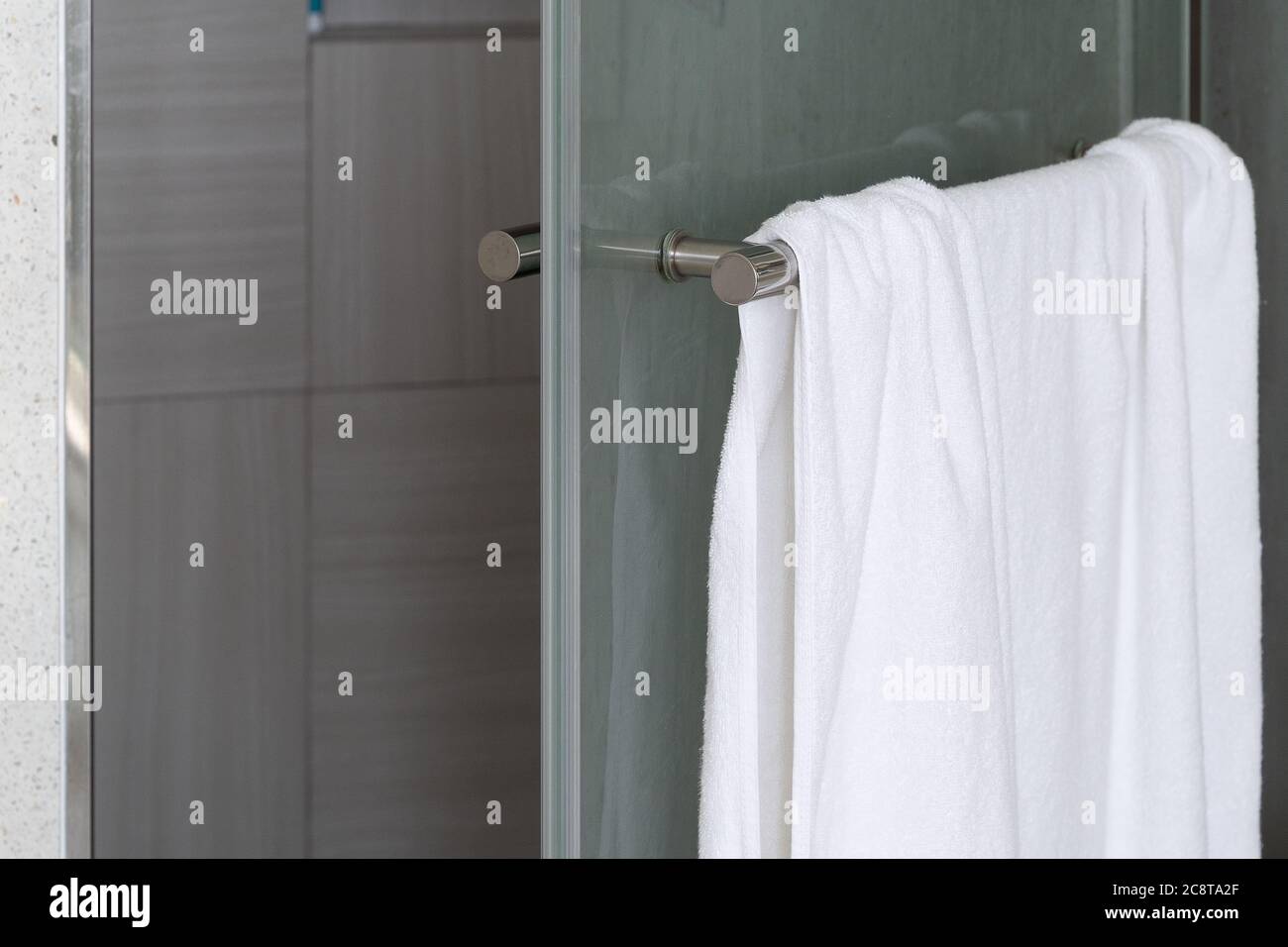 Primo piano. Un asciugamano bianco e pulito è appeso alla parete in cemento esposta del bagno. Foto Stock