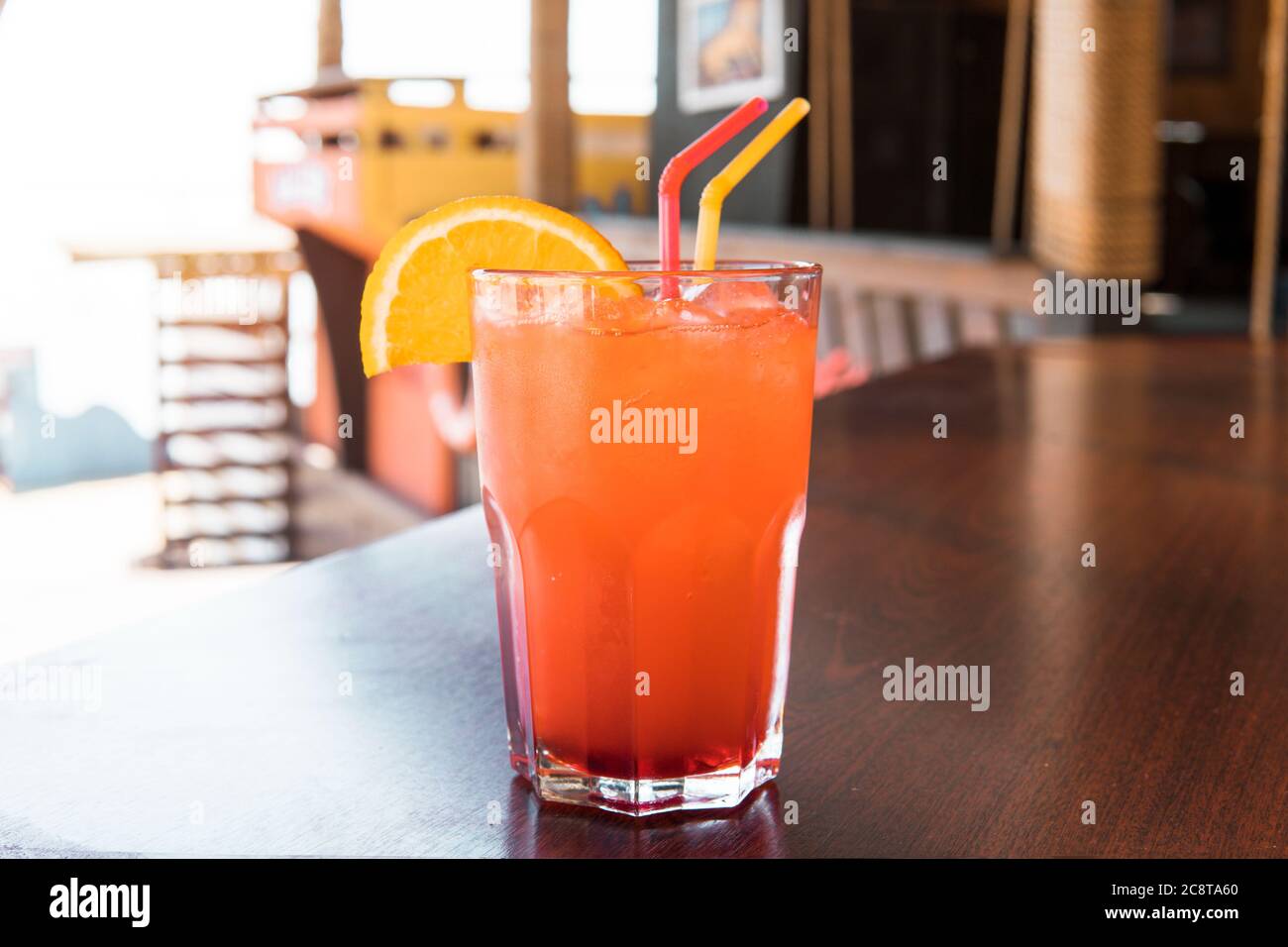 Un bicchiere di succo rosso su un tavolo di legno. Una coda d'urto da closeup di una bevanda dolce al whisky di bourbon guarnita con buccia d'arancia sulla cabina del tavolo con bokeh sfocato Foto Stock