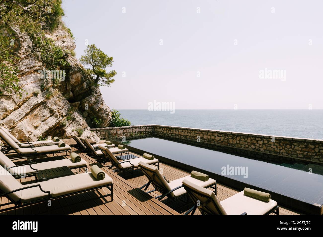 Lettini abbronzanti a bordo piscina sull'isola Sveti Stefan con vista sul mare. Foto Stock