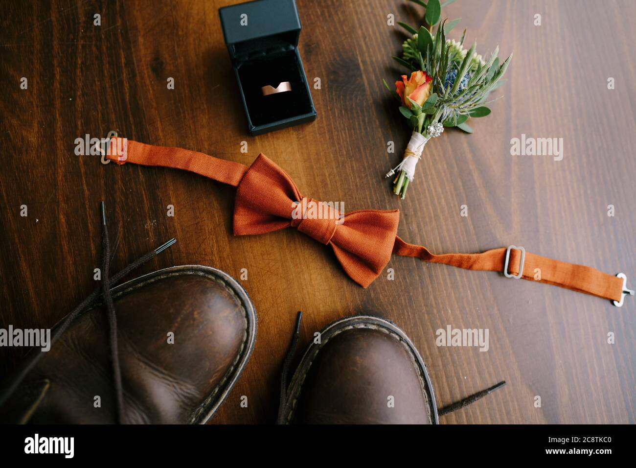 Primo piano della cravatta con boutonnière, anello di aggancio uomo in una scatola e stivali da uomo sul pavimento marrone. Foto Stock