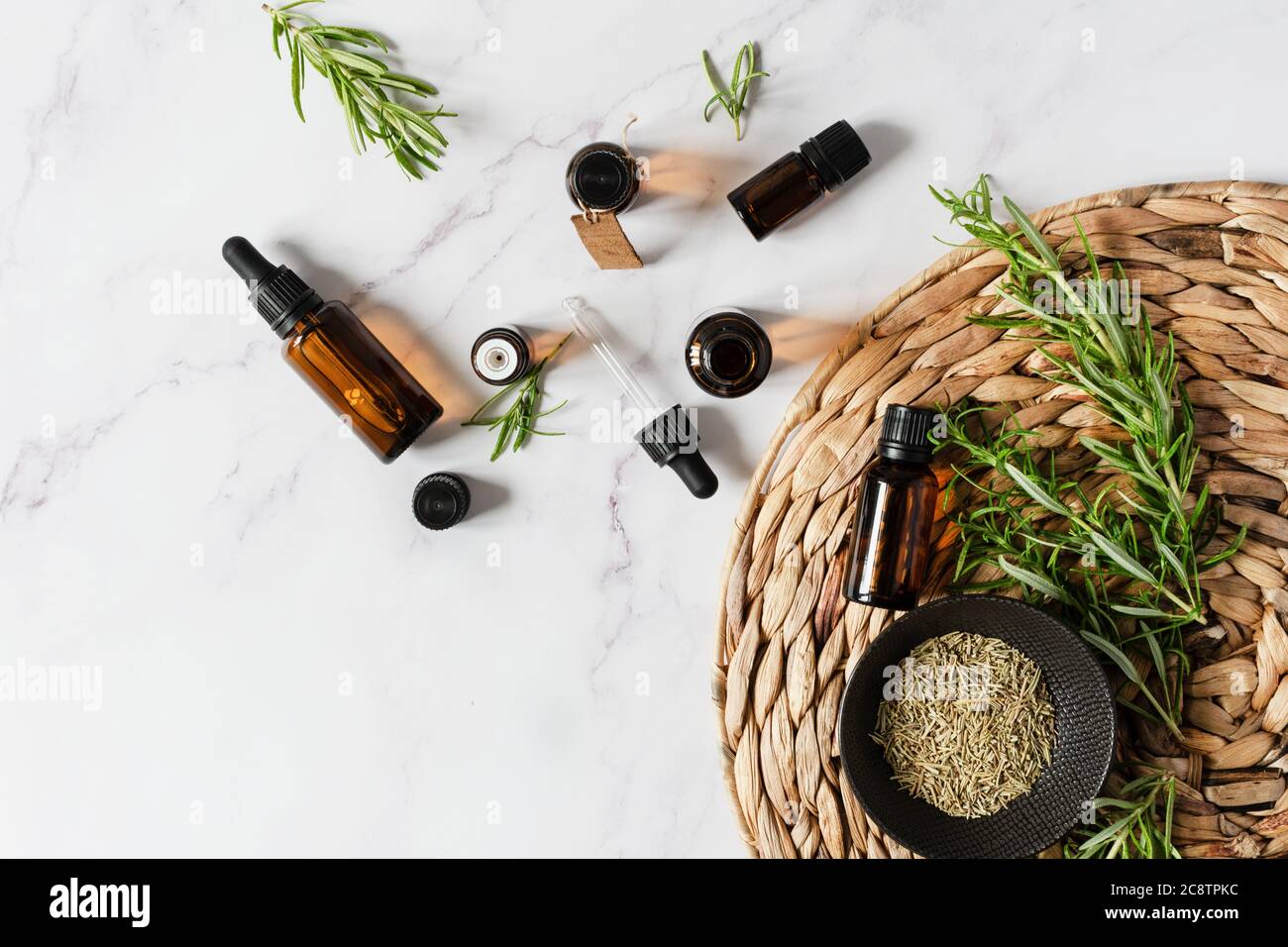 Bottiglie di olio essenziale di rosmarino e ramificazione di rosmarino fresco su sfondo bianco di marmo vista dall'alto. Foto Stock