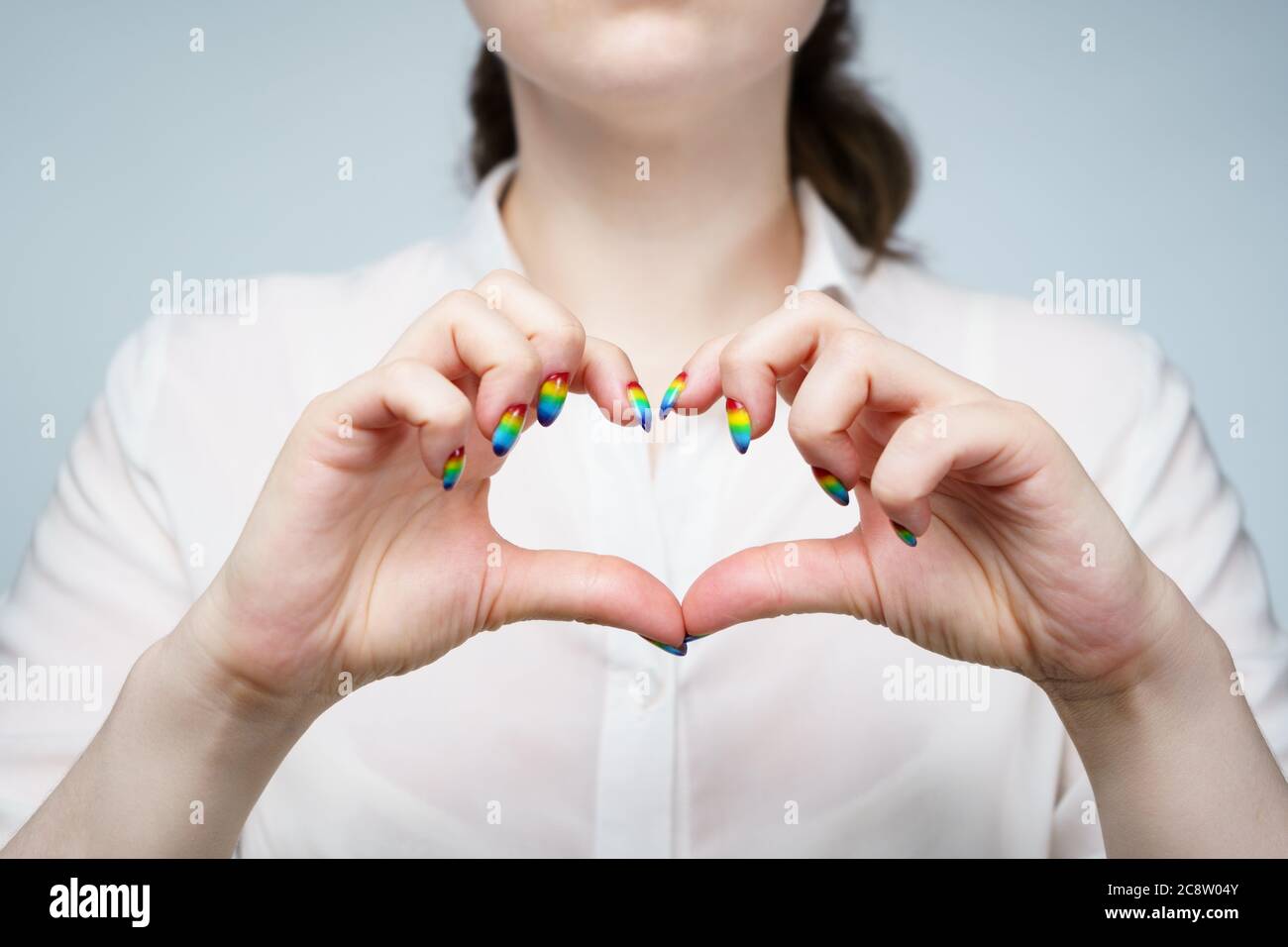 Foto di donna con manicure arcobaleno che mostra il cuore Foto Stock