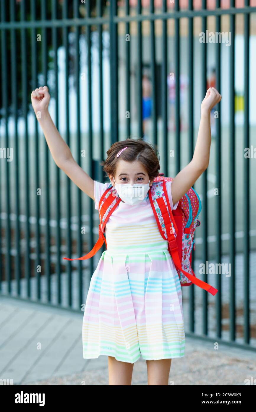 La ragazza che indossa una maschera prende un salto per la gioia a tornare a scuola. Foto Stock