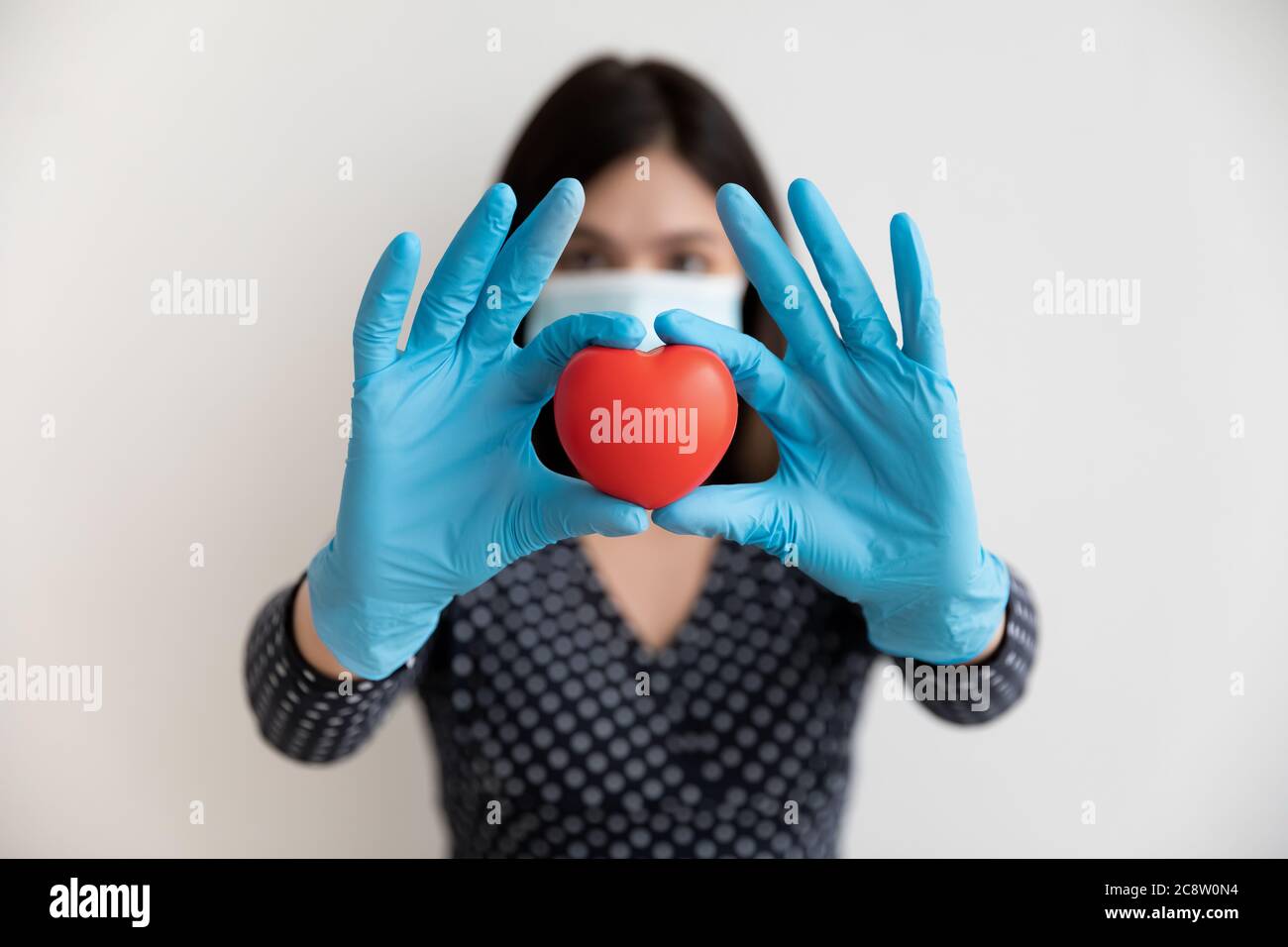 Primo piano di donna in maschera mostra giocattolo cuore rosso Foto Stock