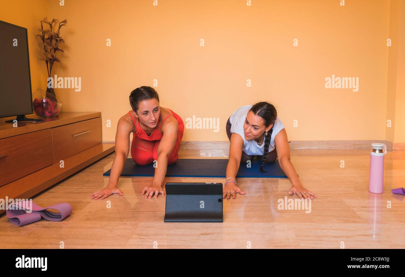 Lezioni di yoga e-learning tablet a casa durante il coronavirus. Due ragazze in forma che controllano le lezioni di yoga e-learning su tablet. Foto Stock