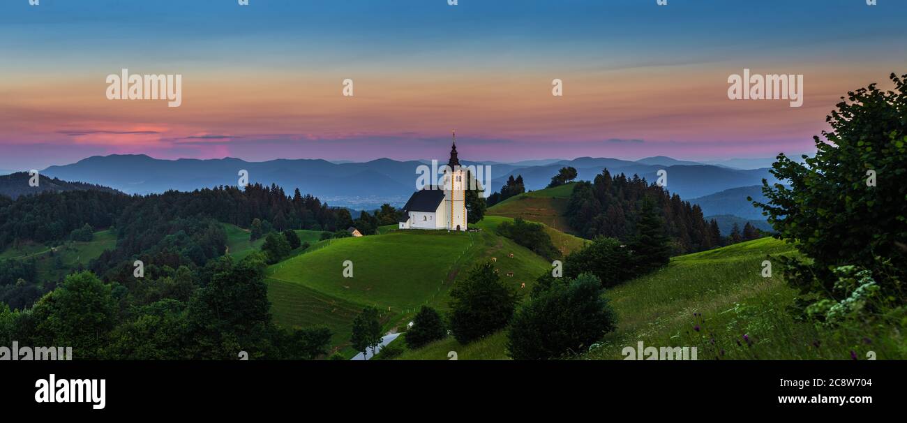 Sveti Andrej, Slovenia - Vista panoramica della chiesa di Sant'Andrea (Sv. Andrej) al tramonto nella zona di Skofja Loka con le Alpi Giulie e il cielo colorato a backgro Foto Stock