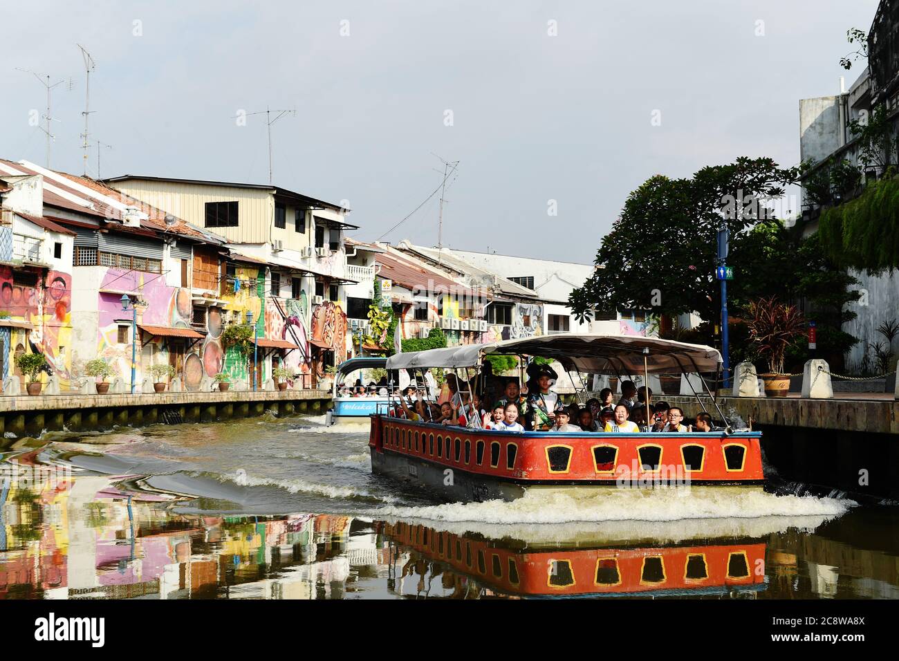 I bambini delle scuole saltano da una barca turistica che naviga lungo il fiume Malacca con opere di Street art sugli edifici sul lungofiume di Malacca Malesia. Foto Stock