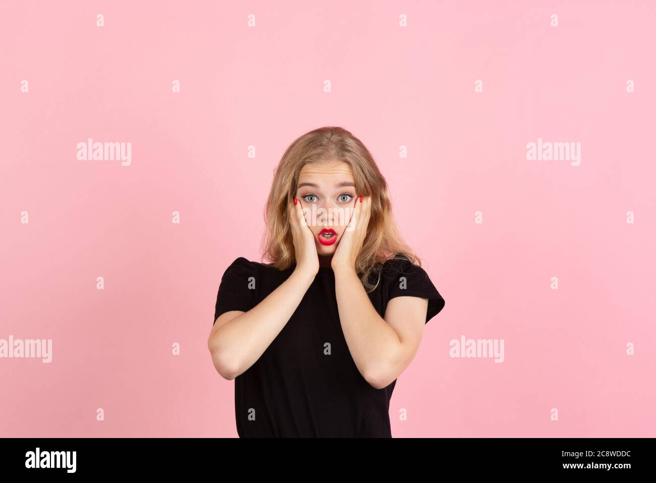 Altamente sconvolto. Ritratto di giovane donna emozionale gesturing isolato su sfondo rosa studio. Emozioni umane, espressione facciale, vendite, concetto di annuncio. Biondo caucasico piuttosto modello gesturing. CopySpace. Foto Stock