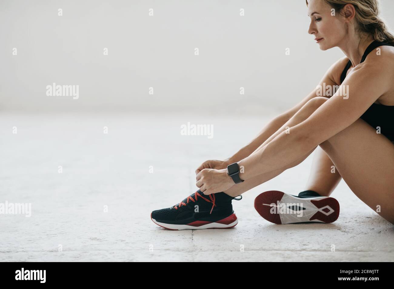 Donna adulta con tracker fitness siede sul pavimento bianco e lacci lacci lacci Foto Stock