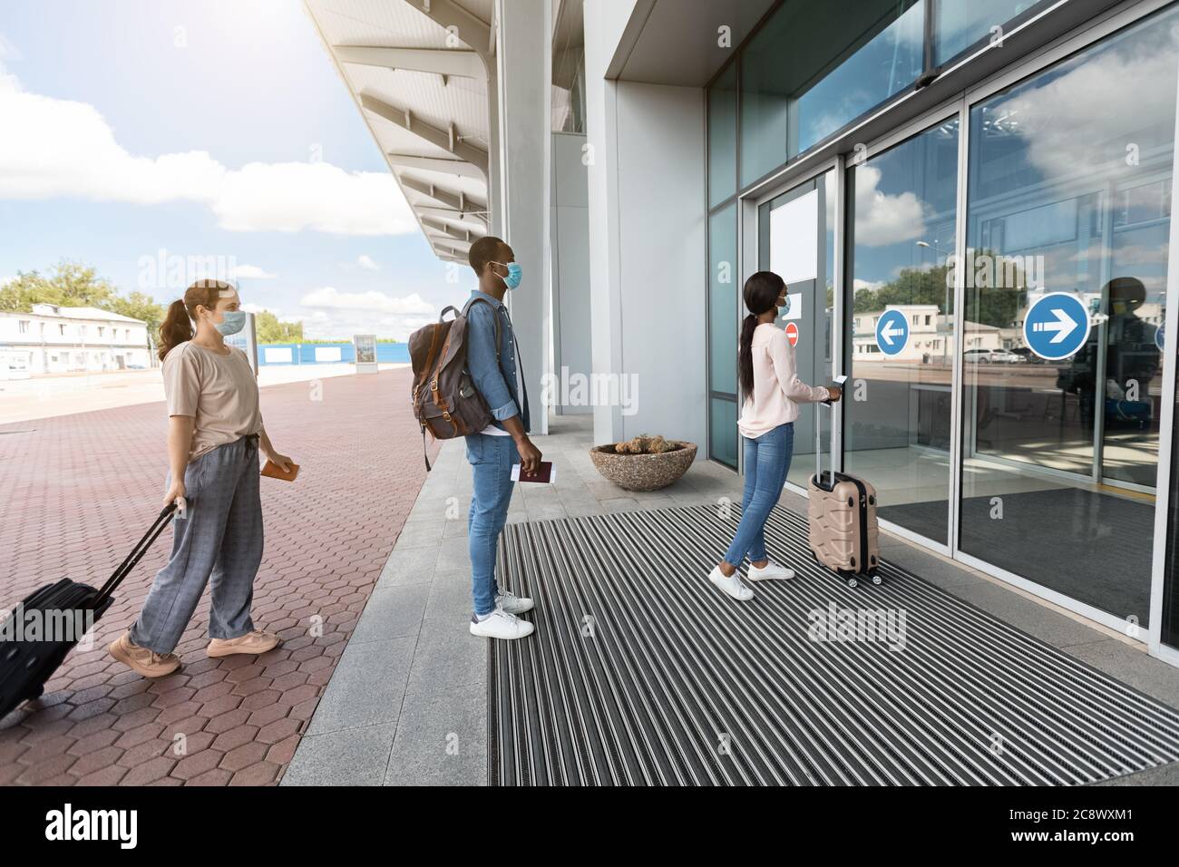 Aeroporto Social Distancing. I passeggeri indossano maschere che si trovano in piedi a turno all'ingresso del terminal Foto Stock