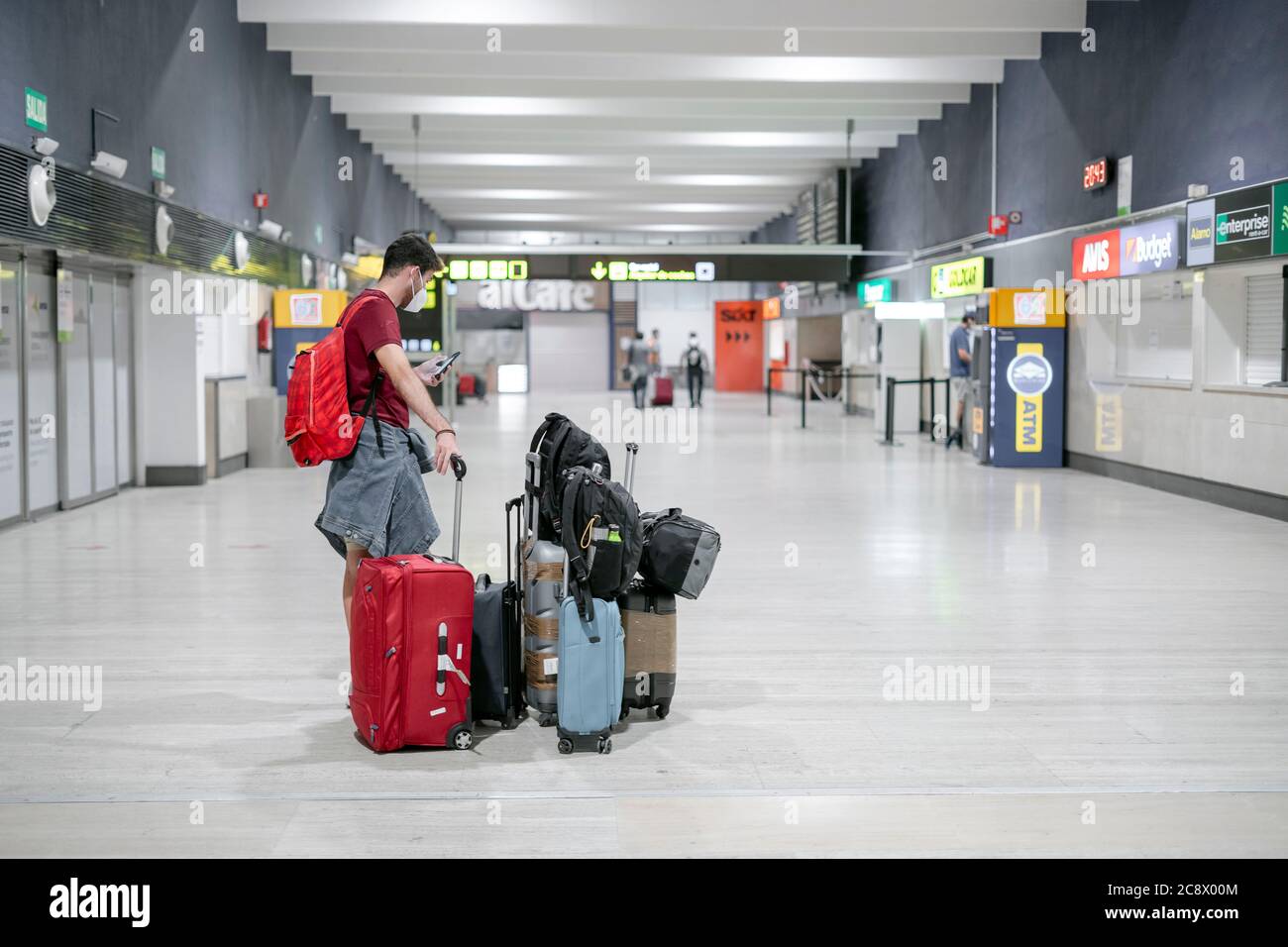 Siviglia, Spagna - 25 luglio 2020: Uomo che indossa una maschera in attesa all'aeroporto con molti bagagli. Foto Stock