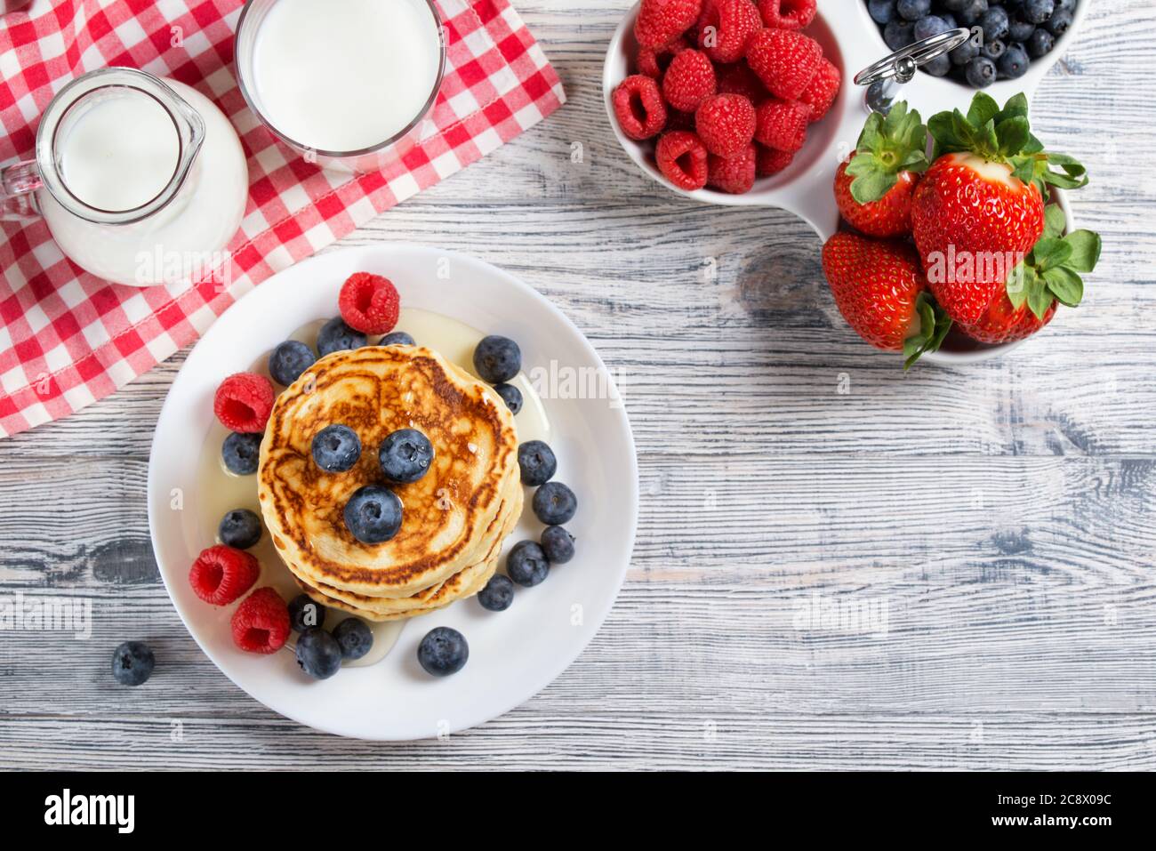 Pila di frittelle con mirtillo fresco, lampone e miele, latte e frutti di bosco freschi, sano concetto di colazione, vista superiore Foto Stock