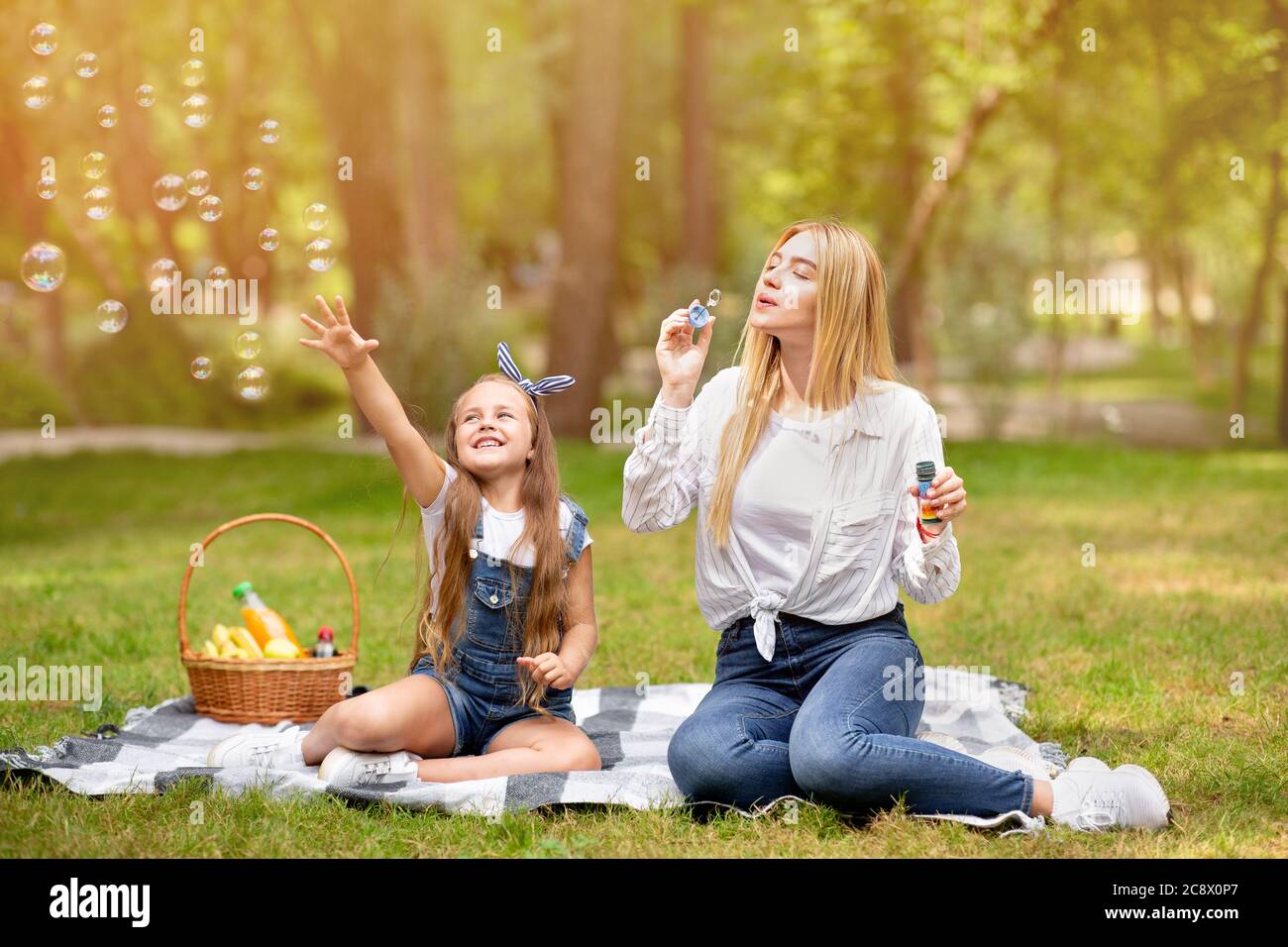 Madre e figlia sul picnic avendo divertimento che soffia le bolle all'aperto Foto Stock
