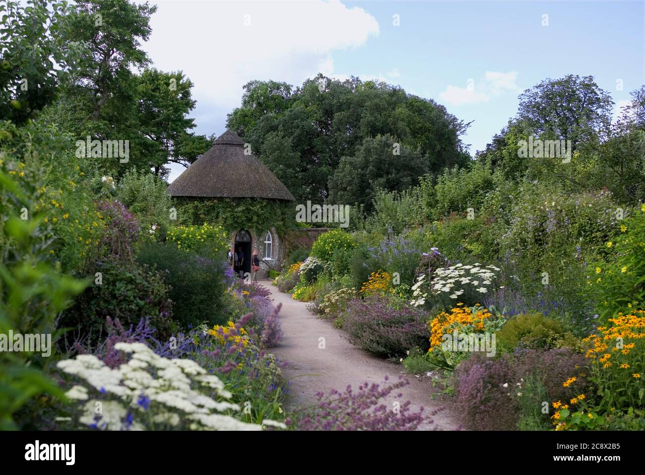 I visitatori dei Walled Gardens, con una casa estiva rotonda con tetto in pietra e pietra, West Dean, West Sussex, Inghilterra, Regno Unito Foto Stock