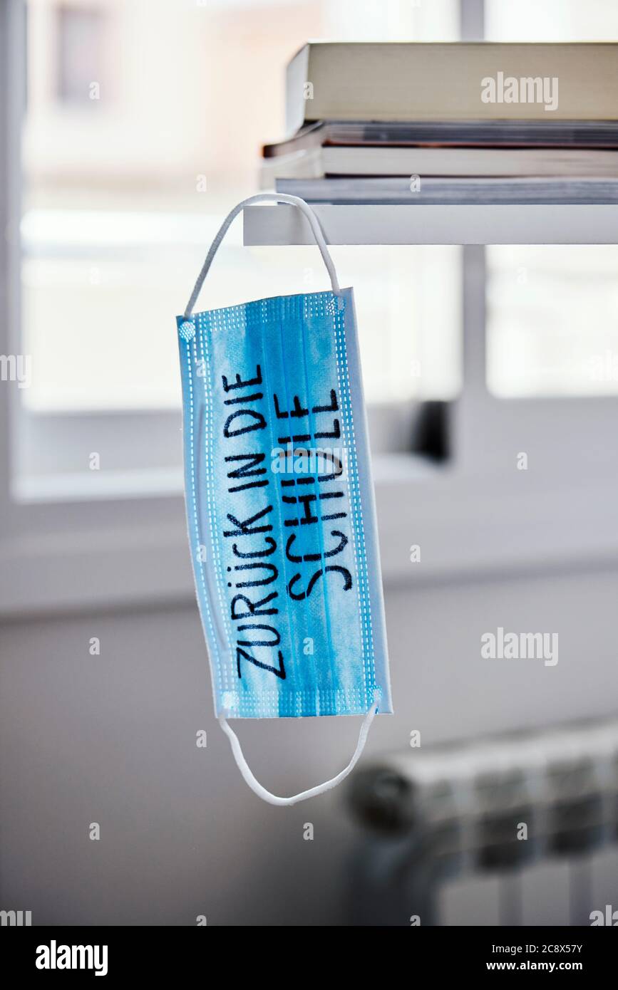 primo piano di una maschera chirurgica blu, su un tavolo, con il testo di ritorno a scuola scritto in tedesco, che raffigura la necessità di prevenire l'infezione a scuola in Foto Stock