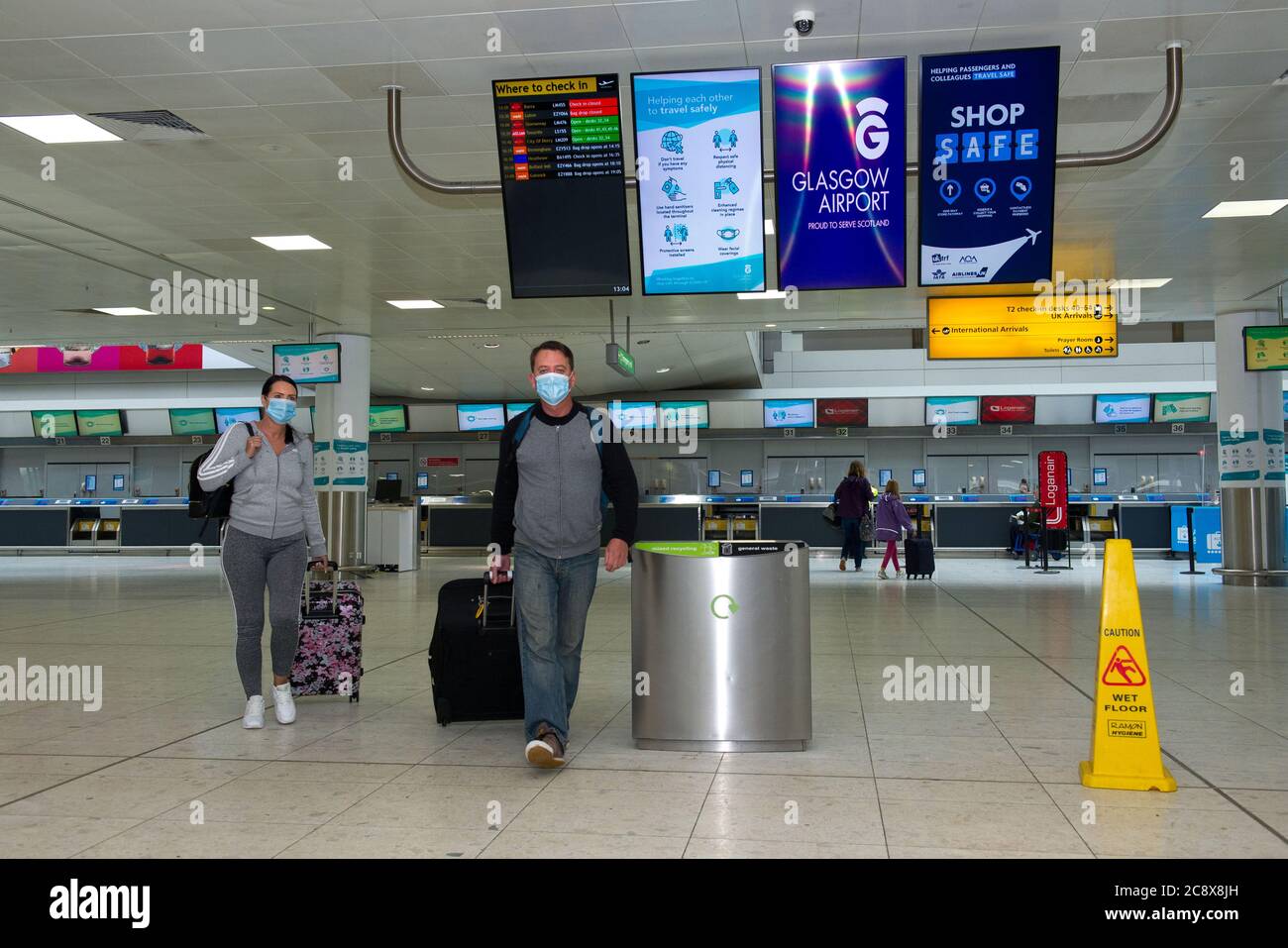 Glasgow, Scozia, Regno Unito. 27 luglio 2020. Nella foto: I passeggeri che indossano maschere chirurgiche blu hanno visto sgranare i bagagli nel terminal dell'aeroporto. All'interno del terminal 1 dell'aeroporto di Glasgow. Il governo scozzese ha annunciato, a partire dalle 00:01 di questa mattina, che tutti i voli in arrivo dalla Spagna verso la Scozia avrebbero bisogno di un periodo di quarantena di 14 giorni. La Jet2 Airlines ha operato una serie di voli questa mattina e un ulteriore servizio pomeridiano per Tenerife, nonostante le nuove restrizioni di viaggio. Credit: Colin Fisher/Alamy Live News Foto Stock