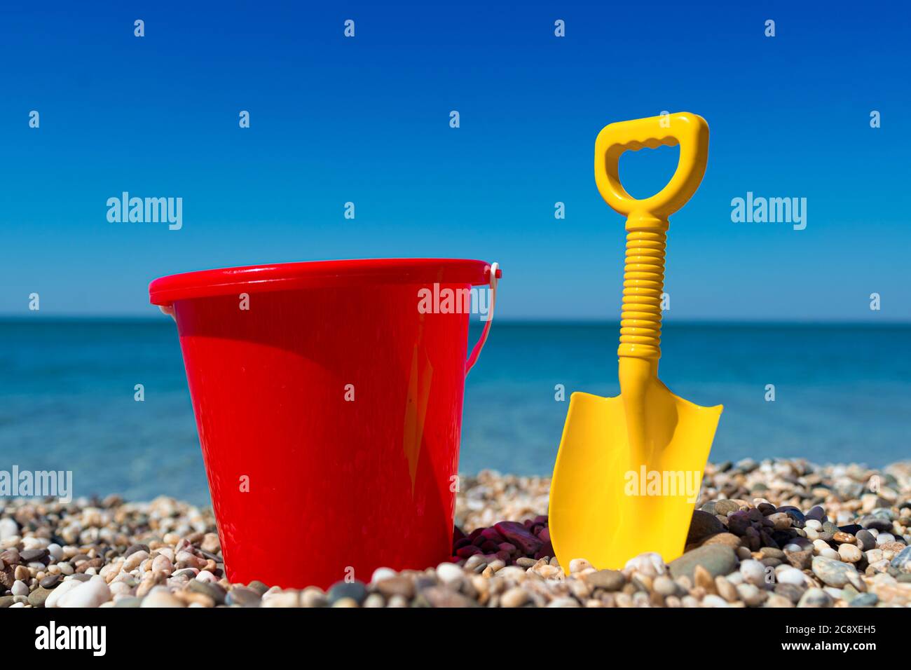 Secchio giocattolo e vanga sulle pietre della spiaggia Foto Stock