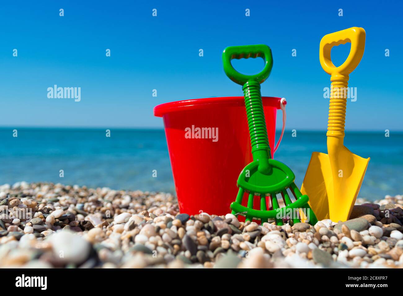 Secchio giocattolo e vanga sulle pietre della spiaggia Foto Stock