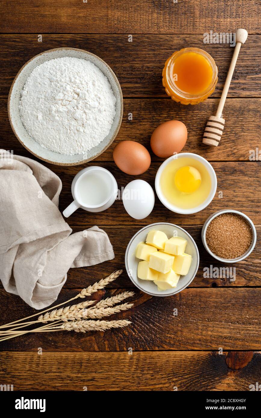 Ingredienti per cuocere su un tavolo di legno. Farina uova zucchero burro e miele. Orientamento verticale, foto rustica del cibo. Piatto posato cucina cibo Foto Stock