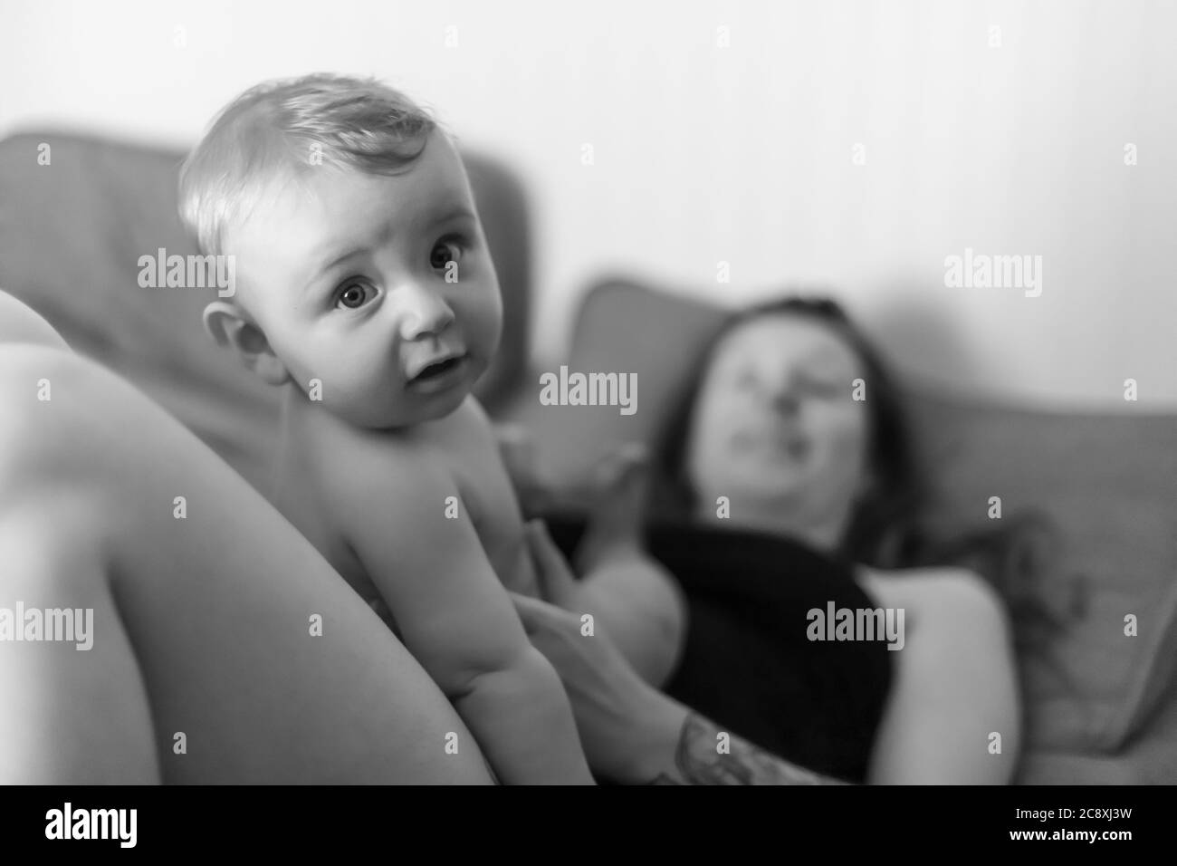 Madre e figlio del bambino intimità gioiosa. Bambino seduto sul ventre della madre e guardando la macchina fotografica con un'espressione divertente. Ritratto in bianco e nero. Foto Stock