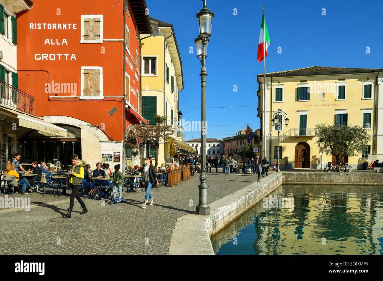 Vista del centro storico sulla riva del Lago di Garda con persone a piedi e seduti in ristoranti all'aperto e il municipio, Lazise, Veneto, Italia Foto Stock